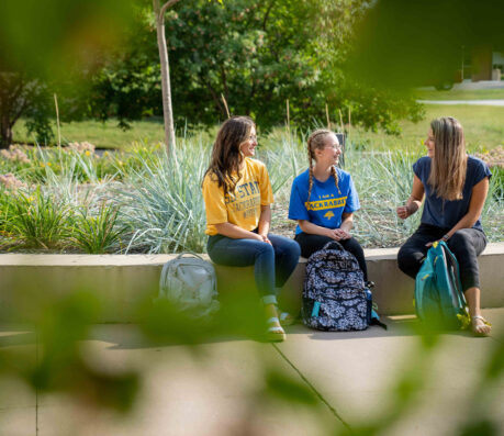 Three SDSU students sit outside the Rotunda chatting between classes.