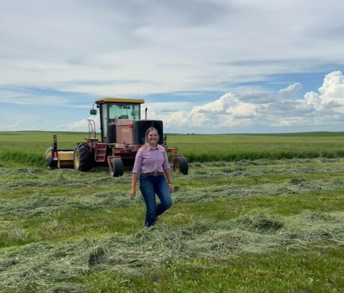 Abby stands in a field with a beautiful blue sky and a tractor behind her.