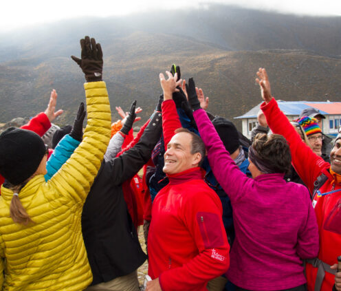Dick Deming high-fiving others in a group at the base of a mountain