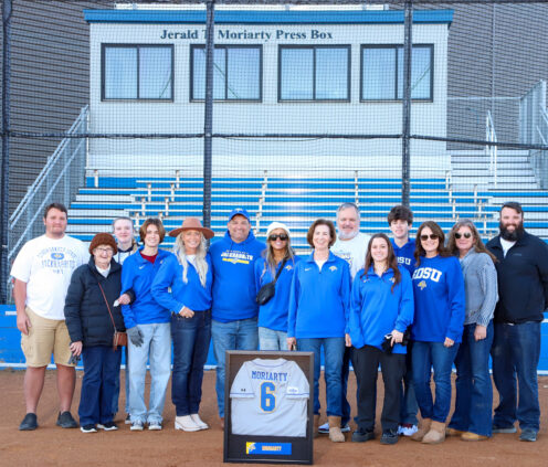 Kevin Moriarty and family stand behind home base with the Jerald Moriarty Press Box in the background