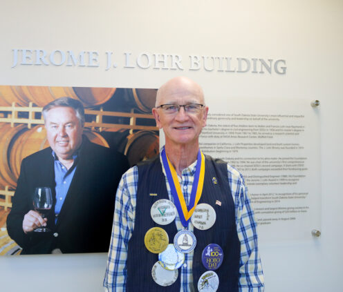 Gordon Niva stands smiling in front of a sign featuring Jerry Lohr shortly after Gordon received the Lohr Award for Volunteer Leadership