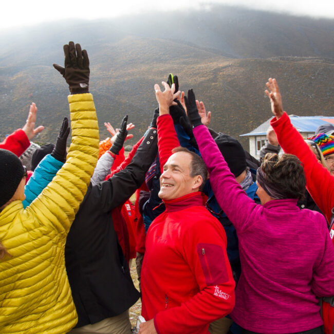 Dick Deming high-fiving others in a group at the base of a mountain
