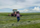 Abby stands in a field with a beautiful blue sky and a tractor behind her.