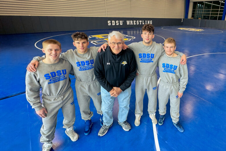 Clay Carlson, Daniel Kimball, Frank Kurtenbach, Cade DeVos, and Tanner Jordan pose for photo on the mats in the Kurtenbach Family Wrestling Center