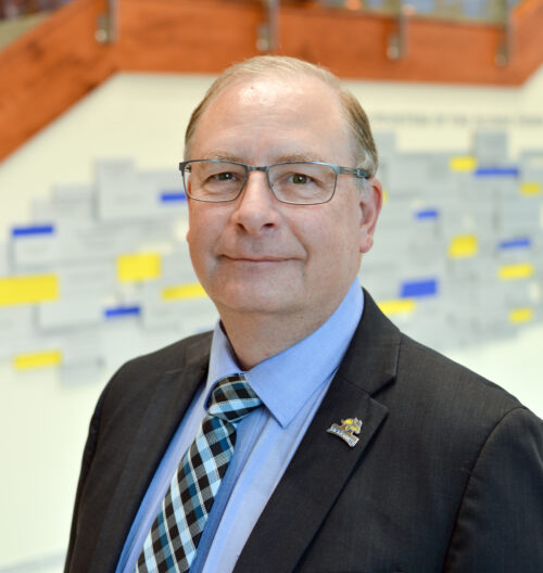 Professional headshot of David Hecht, with blue and yellow blurred background.