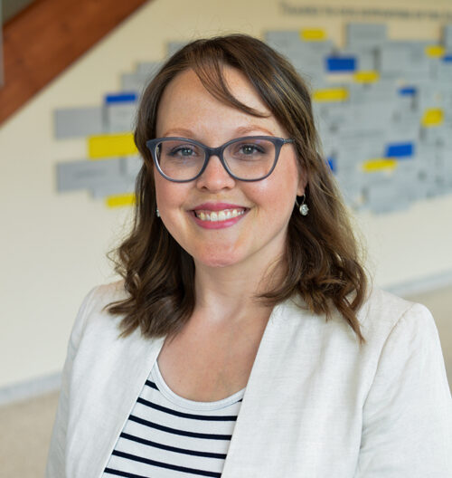 Professional headshot of Holly Tilton Byrne, with a blue and yellow blurred background.