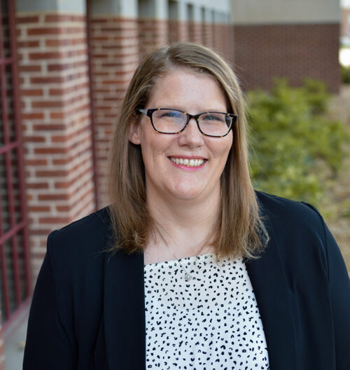 Professional headshot of Jennifer Benson, with blurred landscape background.