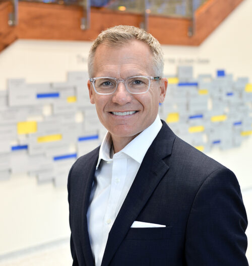 Professional headshot of Keith Mahlum, with blue and yellow blurred background.