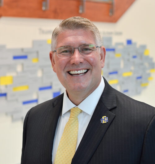 Professional headshot of Mike Birgen, with a blurred blue and yellow background.