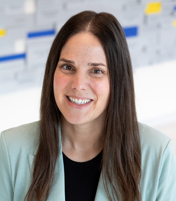 Headshot photo of Brandi Haraldson with a grey, blue, and yellow blurred background