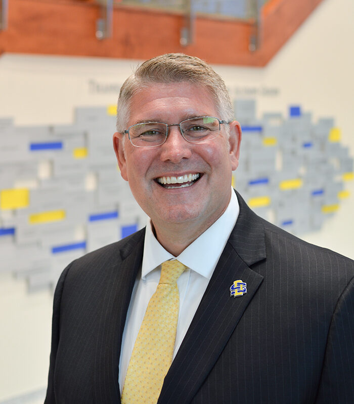 Professional headshot of Mike Birgen, with a blurred blue and yellow background.