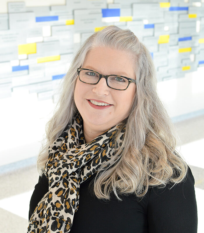 Headshot of Pam Olson with a white, blue, and yellow background.