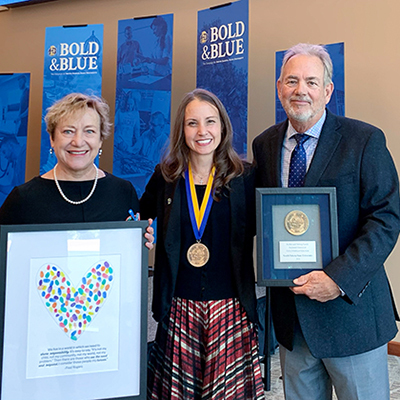 Mary DeJong holding a personalized gift, Dr. Carie Green with her medallion around her neck and Tate Profilet holding a framed medallion all smile for a photo after the investiture ceremony.