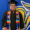 Robert stands, smiling in front of a large Jackrabbit painted on the wall, dressed in a graduation cap and gown, with multiple cords and a colorful stole.