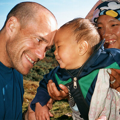 Dick Deming touches lovingly touches foreheads with a smiling baby from Nepal, with the babies mother smiling in the background.