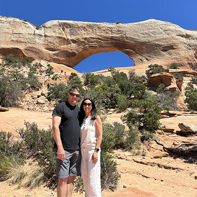 Tom Nieman and his wife smile in front of a stone arch landscape.