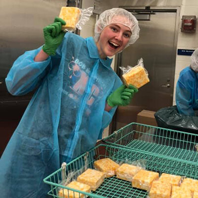 Smiling dairy student holding up packaged cheese.