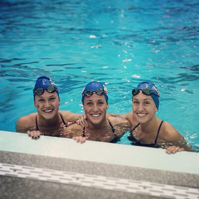 Cassie Hendricks in a pool, smiling with two other female teammates.
