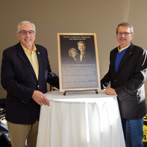 President Dunn and President Emeritus David Chicoine smile while standing next to the plaque that will be hung in honor of Chicoine.