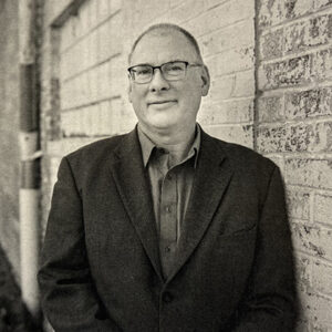 Black and white photo of Steven Wingate, leaning up against an old brick building.
