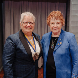 Mary Anne Krogh wears her endowed position medallion, while smiling and standing next to a smiling Roberta Olson.