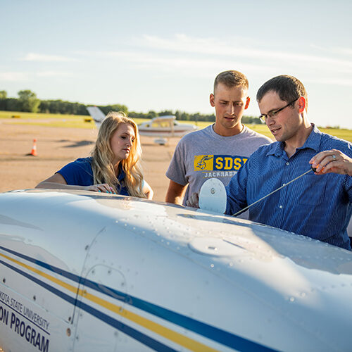 Dr. Cody Christensen stands with two SDSU aviation students, looking over one of the programs planes.
