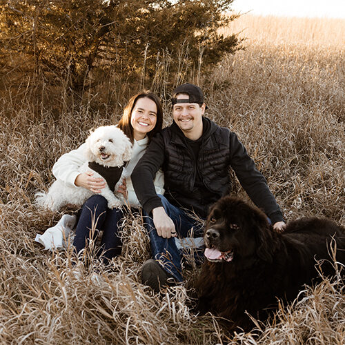 Emily Punt smiles with her husband and two dogs in a field
