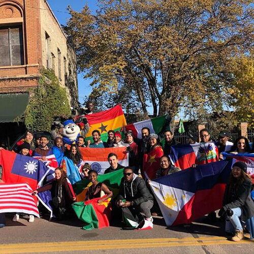 A large group of SDSU students who take part in International Relations Council gather for a group photo, holding flags from countries all over the world.