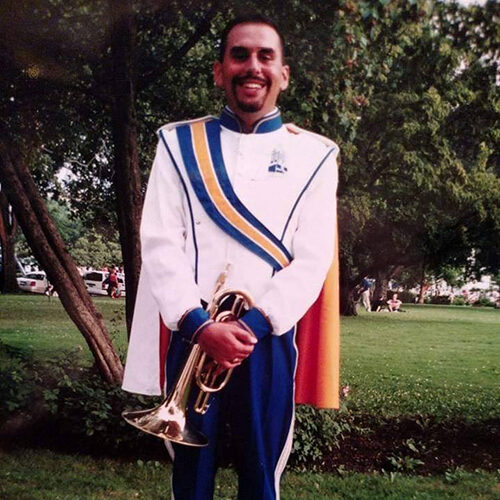 Photo of Kevin Kessler when he was a student member of the Pride of the Dakotas, posing in his uniform, holding an instrument.