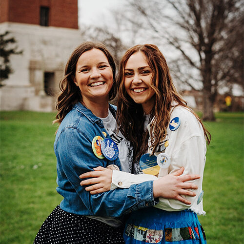 Marissa and a friend smile while embracing each other in a side hug.