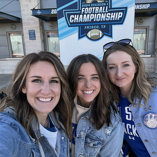 Allison and two other SDSU Foundation team members smiling in front of the FCS Football Championship sign.