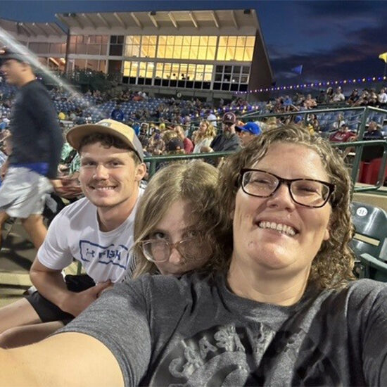 Jennifer Benson holds out the camera in front of her for a selfie photo while her son and daughter sit behind her, smiling for the photo.