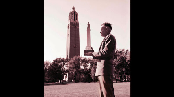 Black and white photo, from 1929, of a man holding a replica of the Coughlin Campanile which is in the background.