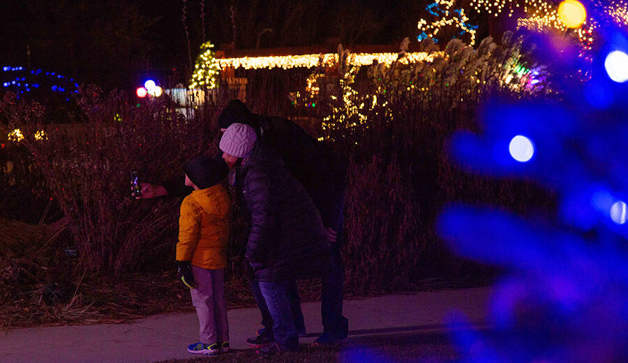 Young family taking a selfie photo with the glowing lights from Garden Glow behind them.