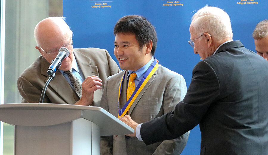Dr. Liu smiling while receiving his medallion from Duane Sander and Al Kurtenbach.