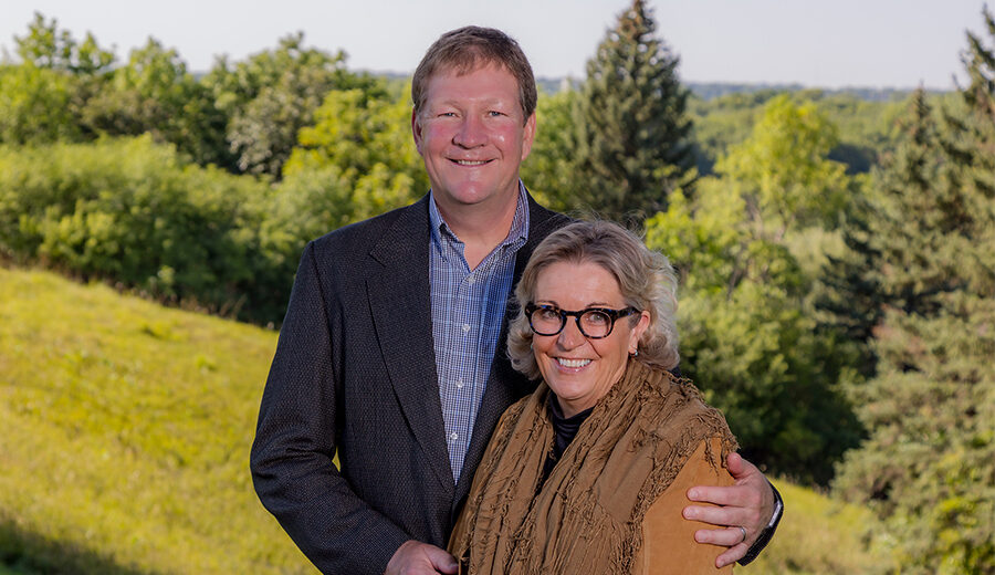 Outdoor photo of Brian and Denise Aamlid, smiling next to one another while Brian has his arm around Denise.