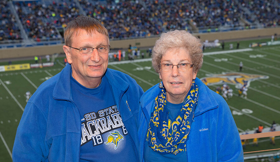 Gary and Sharon Van Riper smile for camera with the SDSU football field in the background