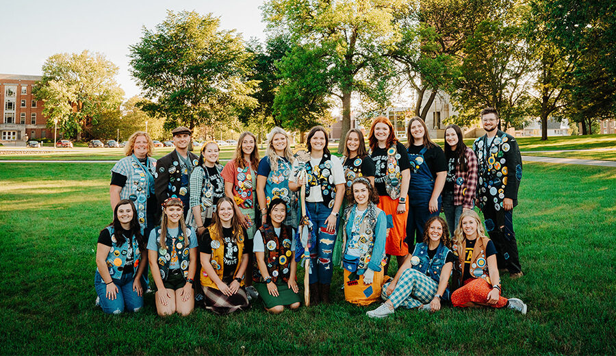 18 members of the Hobo Day committee dressed up in their hobo gear posing together with the Campanile in the background.