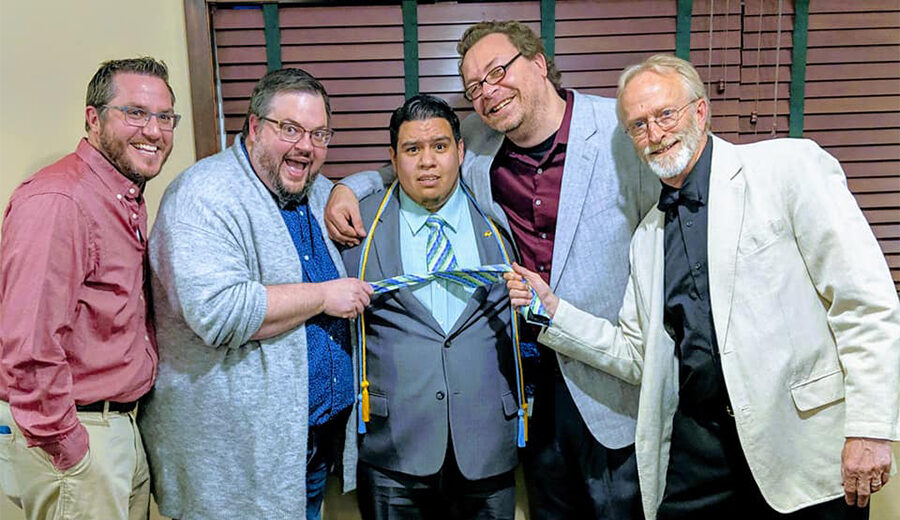 Robert stands in the middle of four South Dakota State University professors/instructors as they all smile while pulling on his tie.